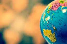 A close-up photograph of a colorful desk globe focused on Southeast Asia, Australia, and the Pacific Ocean, with a warm, blurred background.